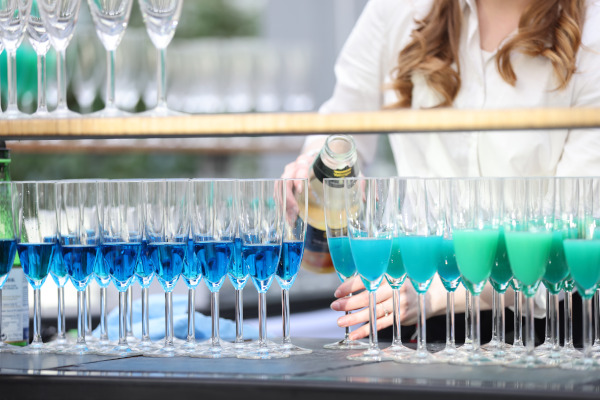 Rückblick auf das pädia Pädiatrie-Event: Eine Servicekraft füllt Sektgläser mit dem eigens kreierten Event-Cocktail "pädia Spritz". Die Gläser leuchten in einem farbigen Farbverlauf von intensivem Blau bis hin zu Türkis und Grün.