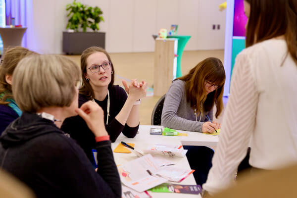 Rückblick auf das pädia Pädiatrie-Event: Vier Teilnehmerinnen sitzen beim PädiaLab an einem Tisch und erarbeiten spielerisch Produktinformationen. Eine Teilnehmerin erklärt lebhaft mit Gesten, eine weitere macht konzentriert Notizen. Auf dem Tisch liegen pädia-Produktbroschüren und Arbeitsmaterialien.