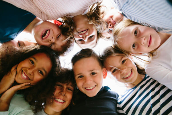 Eine Gruppe lachender Kinder steckt die Köpfe eng zusammen – eine typische Situation für die schnelle Übertragung von Kopfläusen durch direkten Haarkontakt